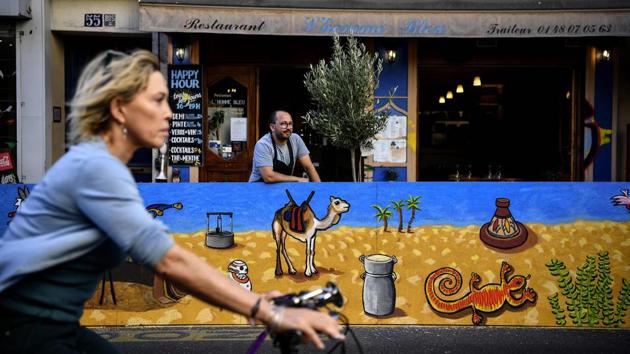 A cyclist rides past a man standing within the extended terrace of a restaurant made of painted wooden pallets in Paris on July 22. While some owners stick with the rough look of raw wood, many others have added splashes of colour and installed plants or small trees and other decorations on their makeshift patios. (Christophe Archambault / AFP)