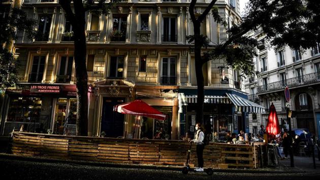 A woman rides an electric scooter past a cafe with an extended terrace in Paris on July 22. And in a country where air-conditioning remains rare, outdoor tables offer an escape from hot homes or restaurant dining rooms. (Christophe Archambault / AFP)