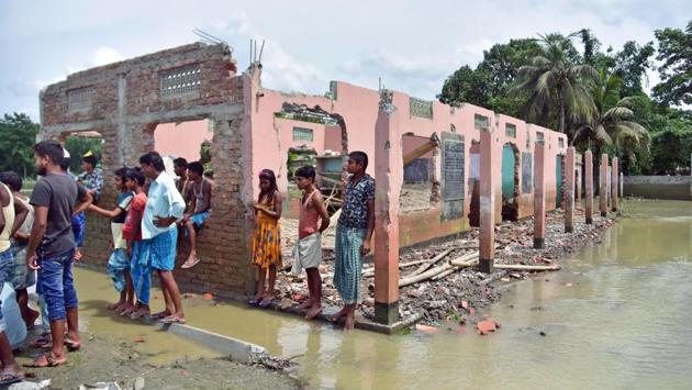 Villagers stand next to part of a school that collapsed due to floodwater at Bhurbandha village in Assam’s Nagaon district on July 25. Union minister for development of north eastern region Jitendra Singh spoke to Assam chief minister Sarbananda Sonowal on July 26 and assured him help from the Centre and the North Eastern Council to restore and repair the infrastructure damaged in floods. (ANI)