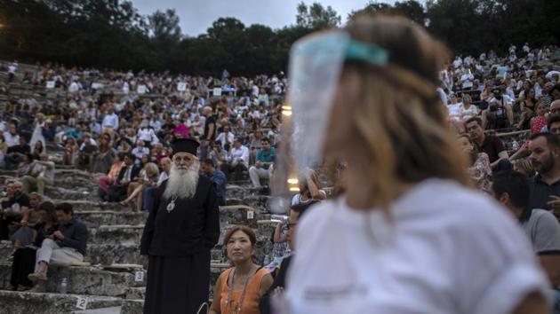 A steward wearing plastic visor stands in front of a Greek Orthodox priest as spectators take their seats at the ancient theatre of Epidaurus, Greece. (AP Photo/Petros Giannakouris) A steward wearing plastic visor stands in front of a Greek Orthodox priest as spectators take their seats at the ancient theatre of Epidaurus, Greece. (AP Photo/Petros Giannakouris)