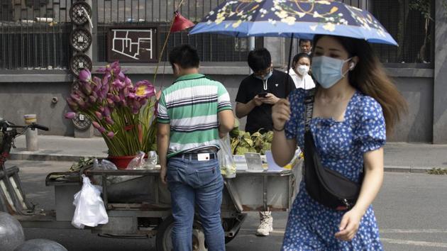 A woman wearing a mask to curb the spread of the coronavirus walks past a street vendor selling lotus flowers and seeds in Beijing on Frida.(AP)