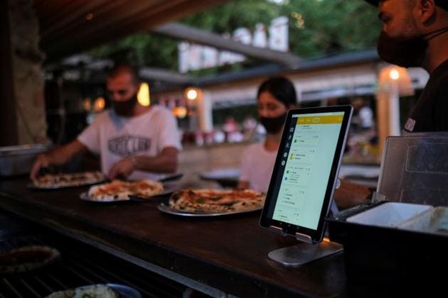 Employees pick up the pizzas near an IPad with the "Funky Pay" app, which helps tracking orders of clients and where, with a system of colours, clients can see when it is in the kitchen or when it will be arriving, at Funky Pizza restaurant, where the app replaces waiters, in Palafrugell, near Girona, Costa Brava, Spain July 31, 2020. Picture taken July 31, 2020. (REUTERS)