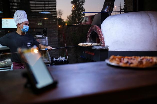 An employee takes a pizza out of the oven after his mate used the "Funky Pay" app, where they receive all the incoming orders of clients, at Funky Pizza restaurant, where the app replaces waiters, in Palafrugell, near Girona, Costa Brava, Spain July 31, 2020. (REUTERS)