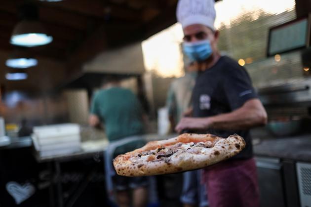 An employee takes a pizza out of the oven after his mate used the "Funky Pay" app, where they receive all the incoming orders of clients, at Funky Pizza restaurant, where the app replaces waiters, in Palafrugell, near Girona, Costa Brava, Spain July 31, 2020. (REUTERS)
