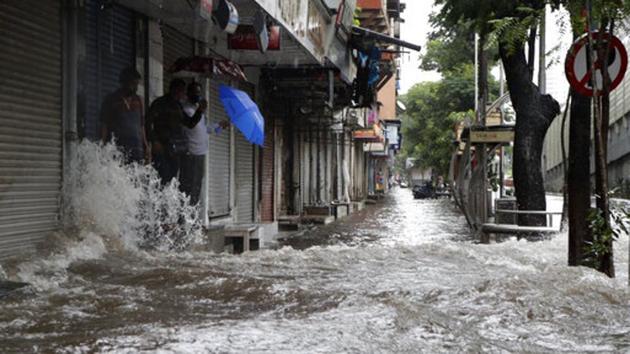 People stand next to a water logged street in Mumbai on August 4. The Brihanmumbai Municipal Corporation (BMC) appealed to residents to stay at home and urged commercial establishments, except those providing essential services, to remain closed on August 4. (Rajanish Kakade / AP)