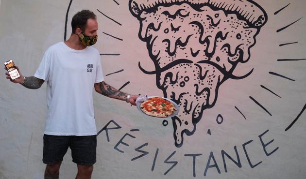 Funky Pizza restaurant owner Carlos Manich poses as he holds his mobile phone with the "Funky Pay" app in one hand and a pizza in the other, at Funky Pizza restaurant, where the app replaces waiters, in Palafrugell, near Girona, Costa Brava, Spain July 31, 2020. (REUTERS)