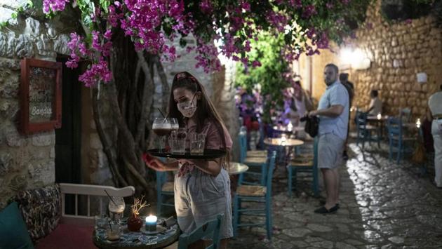 A waiter wearing a face mask prepares a table in a bar in the town of Areopoli on the Mani Peninsula, Laconia, Peloponnese region, Greece on Wednesday July 29, 2020. (Konstantinos Tsakalidis/Bloomberg) A waiter wearing a face mask prepares a table in a bar in the town of Areopoli on the Mani Peninsula, Laconia, Peloponnese region, Greece on Wednesday July 29, 2020. (Konstantinos Tsakalidis/Bloomberg)