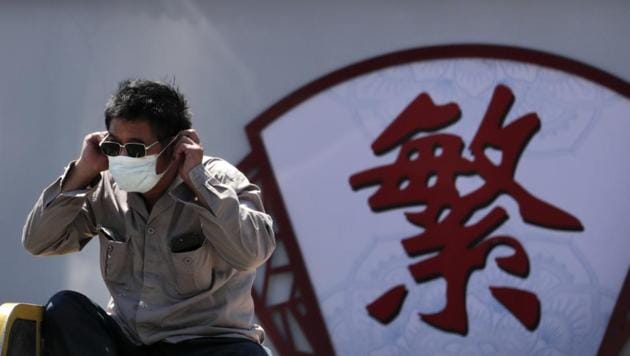 A man puts on his face mask to protect against the new coronavirus as he sits on a tricycle cart passing by the words "Complicated" on a street in Beijing.(AP)