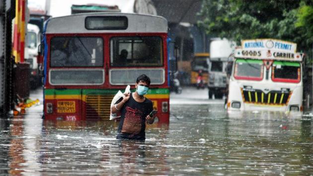 A man crossing a waist-length waterlogged road during rains, in Mumbai on Tuesday.(ANI)