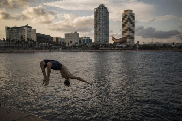 A swimmer jumps into the water from the rocks at the Port Olimpic area of Barcelona, Spain on Sunday, Aug. 2, 2020. Spain’s economy suffered a bigger blow than expected in the second quarter, leaving it with a long recovery that’s become even tougher after a new hit to its vital tourism industry. (Bloomberg)