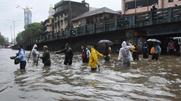 People cross a water logged road while walking in a queue at Byculla in Mumbai on August 5. Several roads like Mahapalika Marg and Colaba Causeway Road in south Mumbai were blocked and closed for commuter movement after trees collapsed due to high-velocity winds in the evening, PTI reported. (Bhushan Koyande / HT Photo)