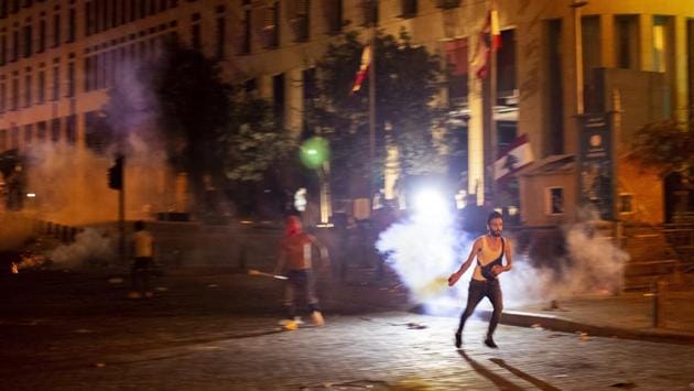 An anti-government protester throws back a tear gas canister fired by the riot police during a protest against the Lebanese political leadership after the massive explosion, in Beirut on August 7. (Hassan Ammar / AP)