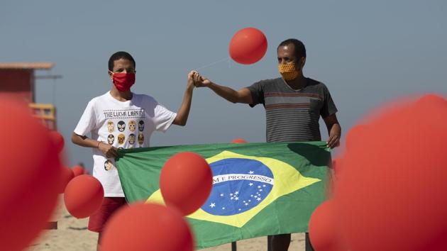 Marcio Antonio do Nascimento, right, and Lucas Cruz, the father and brother of 25-year-old Hugo do Nascimento who died from the new coronavirus, hold a Brazilian national flag as red balloons are released to honor the victims of Covid-19.(AP) Marcio Antonio do Nascimento, right, and Lucas Cruz, the father and brother of 25-year-old Hugo do Nascimento who died from the new coronavirus, hold a Brazilian national flag as red balloons are released to honor the victims of Covid-19.(AP)