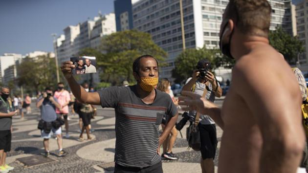 Marcio Antonio do Nascimento, (L), holding a photo of his 25-year-old son Hugo do Nascimento who died from Covid-19, argues with a person who said deaths related to the virus are fake news, during a demonstration to honour victims of the disease, on Copacabana beach in Rio de Janeiro on August 8. (Silvia Izquierdo / AP) Marcio Antonio do Nascimento, (L), holding a photo of his 25-year-old son Hugo do Nascimento who died from Covid-19, argues with a person who said deaths related to the virus are fake news, during a demonstration to honour victims of the disease, on Copacabana beach in Rio de Janeiro on August 8. (Silvia Izquierdo / AP)