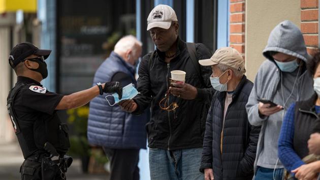 A security officer hands a protective mask to a person waiting in line to enter a Bank of America Corp. branch in San Francisco. The second round of coronavirus-related shutdowns in the country --effective in states like Texas, California and Florida -- are spelling pain for labour markets and portend a deterioration in the overall US employment picture for July. (David Paul Morris / Bloomberg)