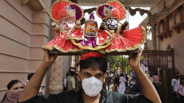 A Hindu devotee wearing a mask carries on his head an idol that depicts Lord Jagannath flanked by sister Subhadra and brother Balram during the annual chariot procession of Lord Jagannath in Ahmedabad.(AP)