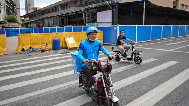 Men ride scooters next to the closed Huanan Seafood Wholesale Market in Wuhan on August 4. Huanan Seafood Market is believed to be the epicentre of coronavirus (COVID-19) disease. It was sealed off by the authorities and still stands empty behind blue barriers. Some vendors have reopened their stalls elsewhere. (Hector Retamal / AFP)