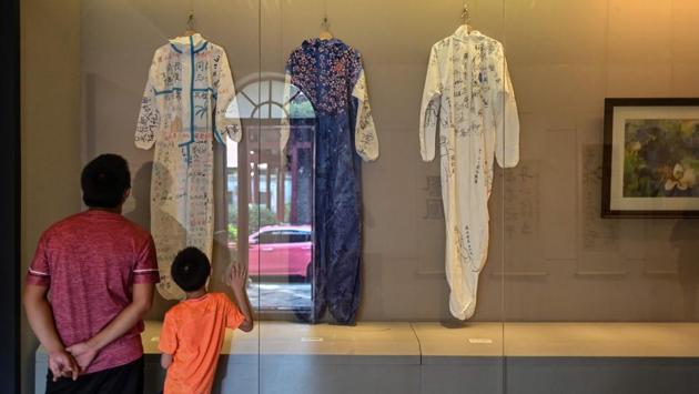 A man and a child peer through glass at autographed Hazmat suits used by medical workers at the height of Wuhan’s outbreak, at a pandemic-themed exhibition--attempted to document the unprecedented period in the city’s history, in Wuhan on August 5. (Hector Retamal / AFP)
