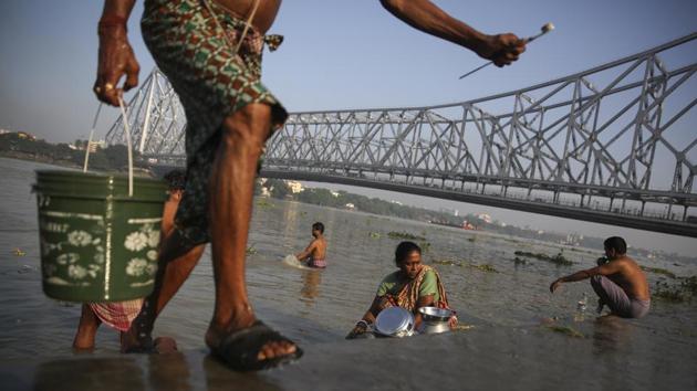 A man carries a bucket of water while people wash utensils, brush their teeth and bathe in the polluted waters of the river Hooghly, in the backdrop of the landmark Howrah Bridge in Kolkata.(AP)