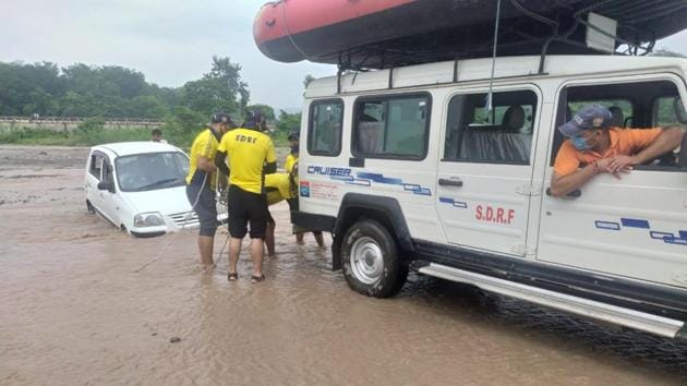 SDRF personnel retrieving a car stuck in water amid heavy rains in Uttarakhand on Wednesday.(HT PHOTO)