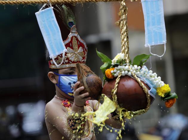 A boy dressed as Hindu god Krishna wears a mask as a precaution against the coronavirus as he breaks a pot during Janmashtami festival celebrations in Mumbai, India, Wednesday, Aug.12, 2020. The festival marks the birth anniversary of Krishna. (AP)