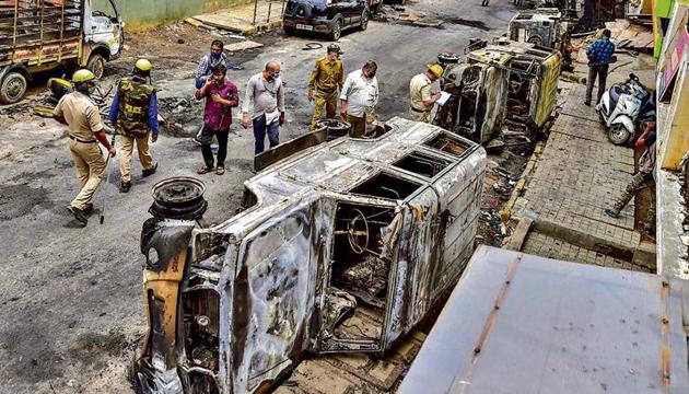 Police and residents walk past charred remains of vehicles vandalised by a mob over a social media post in Bengaluru on Wednesday.