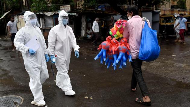 A street vendor selling toys walks past health workers in Mumbai on August 12. The case fatality rate (CFR) for the disease has also declined to 1.98%, HT reported citing government data. (Satish Bate / HT Photo)