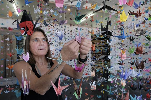 Artist Karla Funderburk, owner of Matter Studio Gallery, adjusts one of of the thousands of origami cranes hanging during an exhibit honoring the victims of COVID-19, Tuesday, Aug. 11, 2020, in Los Angeles. Funderburk started making the cranes three months earlier, stringing the paper swans in pink, blue, yellow and many other colors together and hanging them in her gallery. (AP Photo/Richard Vogel) (AP)