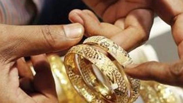 An employee shows gold bangles to a customer at a jewellery showroom in Mumbai nt his file photo. Gold prices are sliding in the international market as well. The US gold futures have fallen by 2.8% to $1,892 an ounce and silver at $23.96 per ounce.(Reuters Photo)