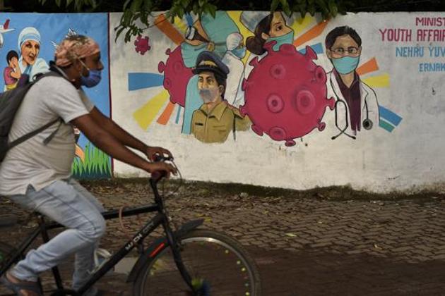 A man wearing a mask pedals his bicycle past a graffiti on a wall made to create awareness about the coronavirus disease (Covid-19) in Kerala’s Kochi in this file photo.(AP)