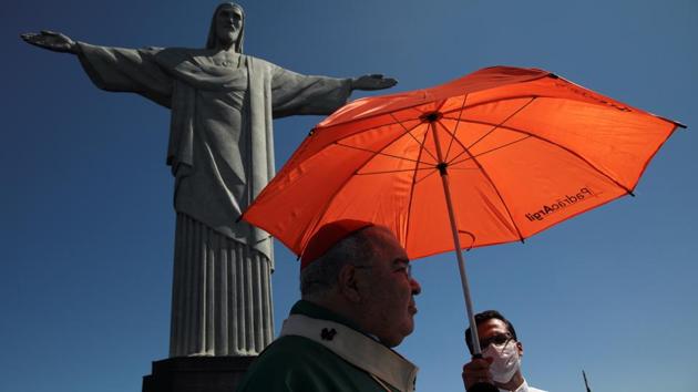An acolyte holds an umbrella over Rio de Janeiro's Archbishop Orani Tempesta to protect him from the sun as he attends a mass in tribute to the victims of the coronavirus disease (COVID-19), on Father's Day, at the Christ the Redeemer statue in Rio de Janeiro, Brazil August 9, 2020. (REUTERS/Ian Cheibub)