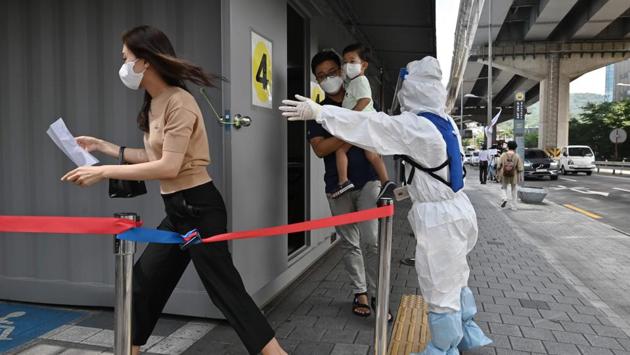 A health official (R) guides visitors at a COVID-19 testing station in Seoul on August 18. “We’re seeing the current situation as an initial stage of a large-scale transmission,” KCDC director Jeong Eun-kyeong told a press briefing. “We’re facing a crisis where if the current spread isn’t controlled, it would bring an exponential rise in cases, which could in turn lead to the collapse of our medical system and enormous economic damage.” (Jung Yeon-je / AFP)