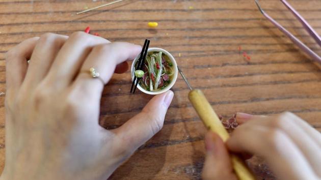 Nguyen Thi Ha An works on a miniature bowl of ‘Pho Ha Noi’ at her studio. Less globally well-known dishes such as sweet rice dessert ‘che com’ are also on the menu at An’s Hanoi studio. But the classics get plenty of attention, with An even modelling tiny bottles of chilli sauce and pickled garlic to accompany her bowls of pho. (Manan Vatsyayana / AFP) Nguyen Thi Ha An works on a miniature bowl of ‘Pho Ha Noi’ at her studio. Less globally well-known dishes such as sweet rice dessert ‘che com’ are also on the menu at An’s Hanoi studio. But the classics get plenty of attention, with An even modelling tiny bottles of chilli sauce and pickled garlic to accompany her bowls of pho. (Manan Vatsyayana / AFP)