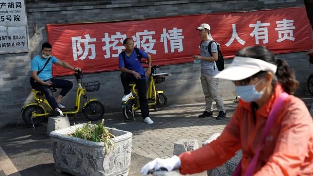 A woman wearing a face mask rides a bicycle past men not wearing face masks on August 21. The Chinese characters on the banner read, "It is everyone’s responsibility to prevent and control the coronavirus disease." (Tingshu Wang / REUTERS)