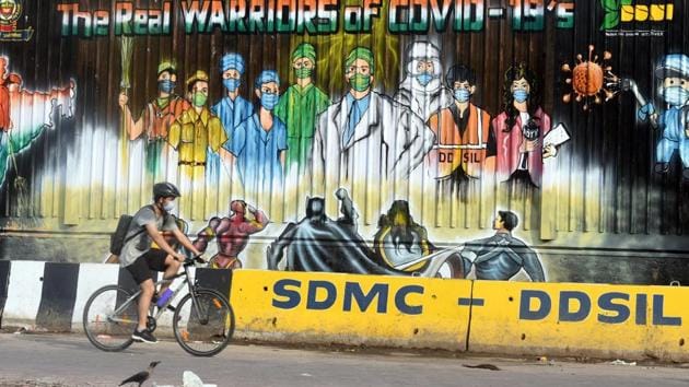 A cyclist crosses a mural reading 'The Real Warriors of Covid-19' honouring coronavirus frontline workers in New Delhi.(Sonu Mehta/HT Photo)