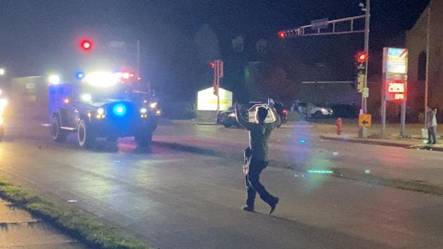 A man with a firearm raises his hands up as he walks towards vehicles during a protest following the police shooting of Jacob Blake, a Black man, in Kenosha, Wisconsin.(Reuters)