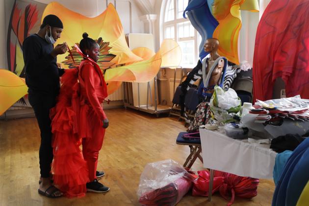 Jez Smith helps Ebony Beckford to get her costume ready for a prepping event ahead of this year's Notting Hill Carnival which will be held virtually, in London, Thursday, Aug. 20, 2020. London's Notting Hill Carnival traces its roots to the emancipation of Black slaves and race riots in the city during the late 1950s. Organizers say the event is more important than ever amid the worldwide campaign for justice following the death of George Floyd in police custody. But their message of resistance and reconciliation will be delivered online worldwide this weekend after the COVID-19 pandemic forced the party to reinvent itself as a virtual event. (AP Photo/Kirsty Wigglesworth) (AP) Jez Smith helps Ebony Beckford to get her costume ready for a prepping event ahead of this year's Notting Hill Carnival which will be held virtually, in London, Thursday, Aug. 20, 2020. London's Notting Hill Carnival traces its roots to the emancipation of Black slaves and race riots in the city during the late 1950s. Organizers say the event is more important than ever amid the worldwide campaign for justice following the death of George Floyd in police custody. But their message of resistance and reconciliation will be delivered online worldwide this weekend after the COVID-19 pandemic forced the party to reinvent itself as a virtual event. (AP Photo/Kirsty Wigglesworth) (AP)