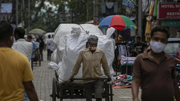 A man wearing a face mask transports good on a cart in Guwahati, India.(AP)