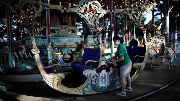 An employee of Toshimaen amusement park wearing a protective mask disinfects a seat of a wooden carousel "Carousel El Dorado" which was built in Germany in 1907 and is believed to be one of the oldest working carousels in the world. (REUTERS/Issei Kato)