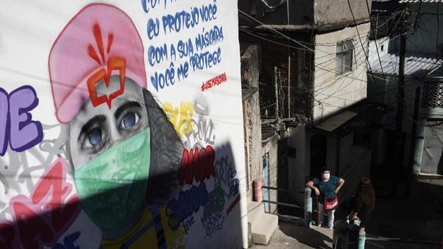 A woman stands next to a mural of a woman wearing a mask that reads in Portuguese “With my mask, I protect you. With your mask, you protect me,” at Morro da Providencia favela in Rio de Janeiro on September 3. Since the end of August, Brazil has averaged around 870 Covid-19 fatalities with 40,000 new infections a day. (Silvia Izquierdo / AP) A woman stands next to a mural of a woman wearing a mask that reads in Portuguese “With my mask, I protect you. With your mask, you protect me,” at Morro da Providencia favela in Rio de Janeiro on September 3. Since the end of August, Brazil has averaged around 870 Covid-19 fatalities with 40,000 new infections a day. (Silvia Izquierdo / AP)