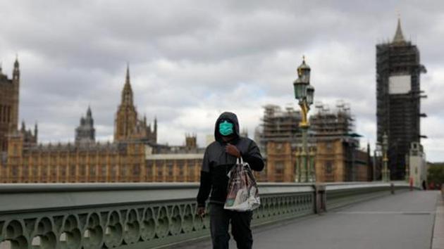 A commuter wearing a protective face mask crosses Westminster Bridge in view of the Houses of Parliament and Elizabeth Tower, also known as Big Ben, in London, UK.(Bloomberg)