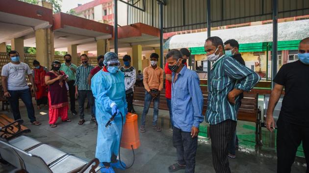 A worker in PPE sprays disinfectant to sanitise an area while people wait their turns to give samples for coronavirus testing, in New Delhi’s Defence Colony area on Wednesday.(Amal KS/HT Photo)