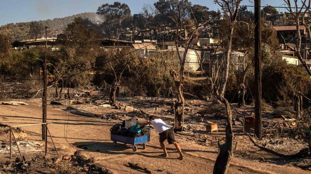 A migrant pushes his belongings past the burnt camp of Moria on September 10. Authorities were already at loggerheads with Lesbos residents over plans to replace Moria with a closed reception centre, which the residents fear would mean thousands of asylum seekers remaining their permanently. (Angelos Tzortzinis / AFP) A migrant pushes his belongings past the burnt camp of Moria on September 10. Authorities were already at loggerheads with Lesbos residents over plans to replace Moria with a closed reception centre, which the residents fear would mean thousands of asylum seekers remaining their permanently. (Angelos Tzortzinis / AFP)