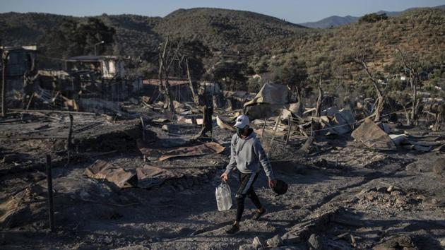 A migrant carries water along the Moria refugee camp in Lesbos, Greece on September 10. Early morning saw former residents of the camp, which had been under coronavirus lockdown, return to the area to pick through the charred remains of their belongings, salvaging what they could. (Petros Giannakouris / AP) A migrant carries water along the Moria refugee camp in Lesbos, Greece on September 10. Early morning saw former residents of the camp, which had been under coronavirus lockdown, return to the area to pick through the charred remains of their belongings, salvaging what they could. (Petros Giannakouris / AP)