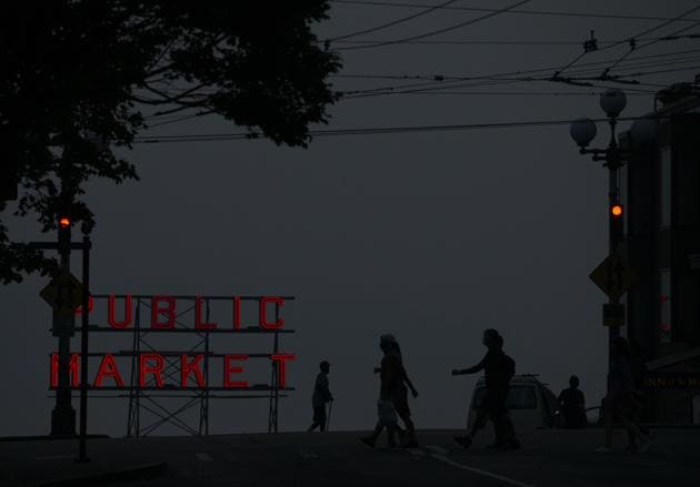 Wildfire smoke obscures the view of Elliott Bay as people walk by a Pike Place Market sign in Seattle, Washington (AFP)