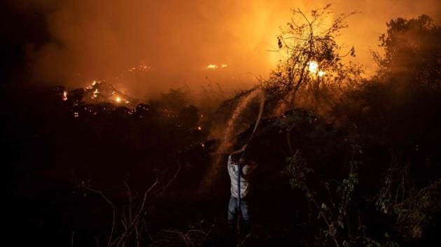 A volunteer throws water to control a fire using a water tank truck to protect a wooden bridge - one of 119 bridges of the Transpantaneira Park Road, on September 13. This massive fire is one of thousands of blazes sweeping the Brazilian Pantanal this year in what climate scientists fear could become a new normal. (Mauro Pimentel / AFP)