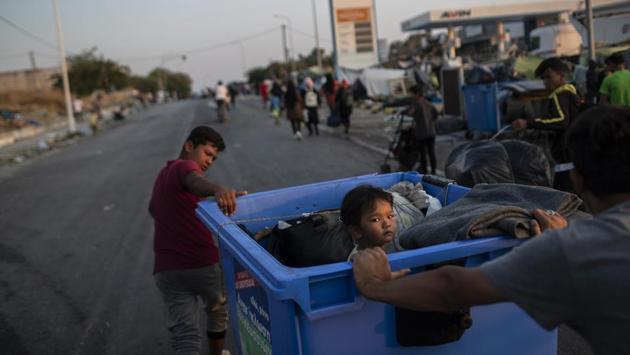 A child sits inside a recycle bin as a boy and man pull their belongings on the island of Lesbos on September 18. “It’s awful, there’s nothing in it, not enough food, toilets, no shower, there’s not even a bed,” Mustafa, a Sudanese asylum seeker, told AFP, after arriving at the temporary camp. (Petros Giannakouris / AP) A child sits inside a recycle bin as a boy and man pull their belongings on the island of Lesbos on September 18. “It’s awful, there’s nothing in it, not enough food, toilets, no shower, there’s not even a bed,” Mustafa, a Sudanese asylum seeker, told AFP, after arriving at the temporary camp. (Petros Giannakouris / AP)