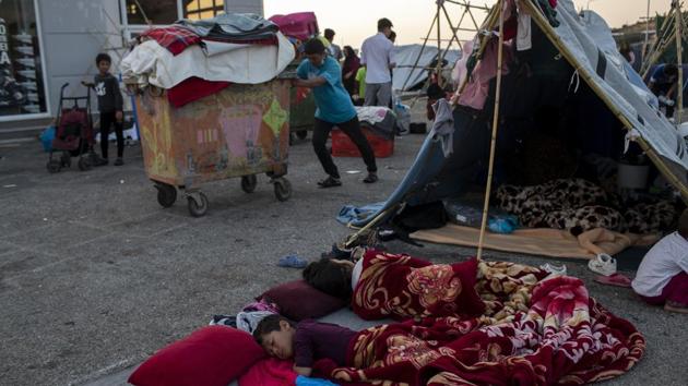 Migrants sleep as another one pushes a trash bin with his belongings on the island of Lesbos on September 18. Many asylum seekers told AFP that they are wary of entering the new camp, or were only doing so out of necessity as they are no longer able to sleep on the street with limited access to food and water. (Petros Giannakouris / AP) Migrants sleep as another one pushes a trash bin with his belongings on the island of Lesbos on September 18. Many asylum seekers told AFP that they are wary of entering the new camp, or were only doing so out of necessity as they are no longer able to sleep on the street with limited access to food and water. (Petros Giannakouris / AP)