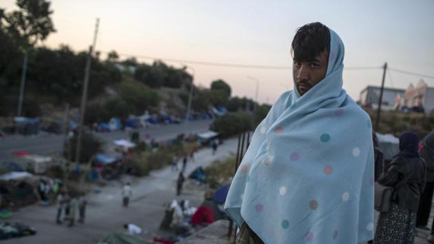 A migrant with a blanket stands on a rooftop of a building during relocation to the new camp on the island of Lesbos on September 17. AFP reported that there were also some refugees who refused to enter the new camp, fearing a temporary settlement would hamper the processing of their asylum requests to mainland Greece or other European countries. (Petros Giannakouris / AP) A migrant with a blanket stands on a rooftop of a building during relocation to the new camp on the island of Lesbos on September 17. AFP reported that there were also some refugees who refused to enter the new camp, fearing a temporary settlement would hamper the processing of their asylum requests to mainland Greece or other European countries. (Petros Giannakouris / AP)