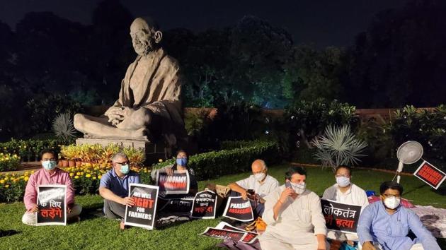 The suspended members of Rajya Sabha sit near the Gandhi statue in Parliament on Monday evening. The suspended members of Rajya Sabha sit near the Gandhi statue in Parliament on Monday evening.
